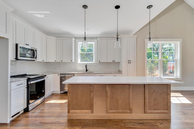 kitchen with appliances with stainless steel finishes, white cabinetry, a healthy amount of sunlight, and a center island