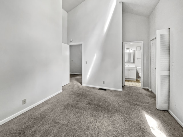 unfurnished bedroom with a closet, high vaulted ceiling, ensuite bathroom, and carpet floors