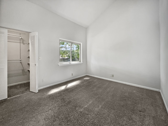 unfurnished bedroom with lofted ceiling, dark colored carpet, and a closet