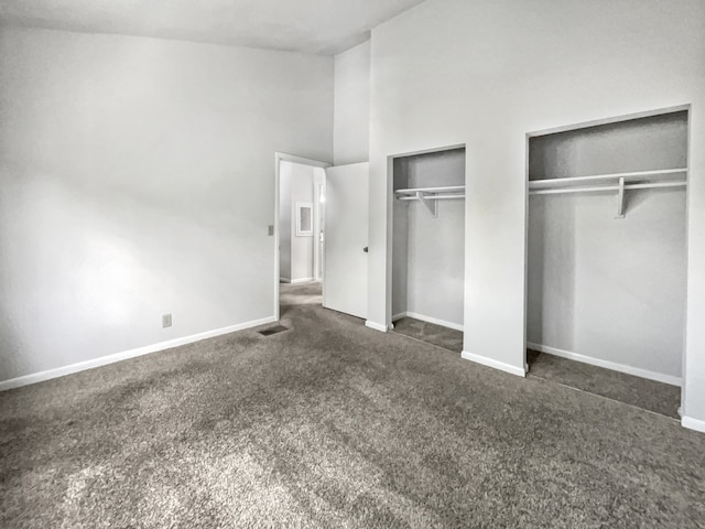 unfurnished bedroom with dark carpet, two closets, and lofted ceiling