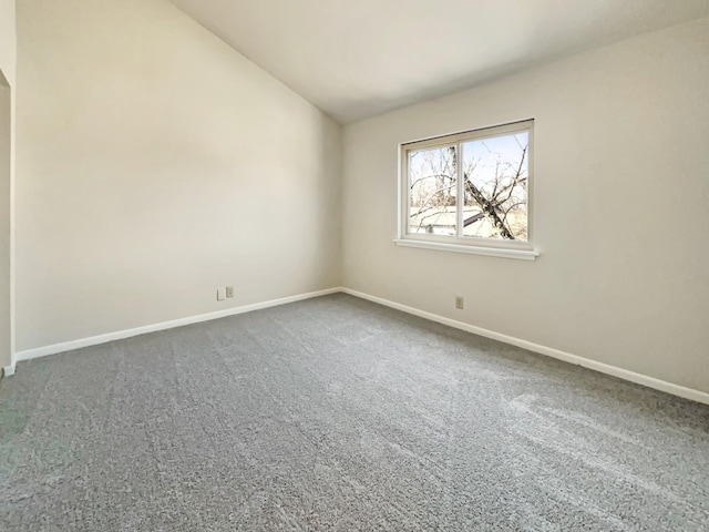 empty room with lofted ceiling, dark colored carpet, and baseboards