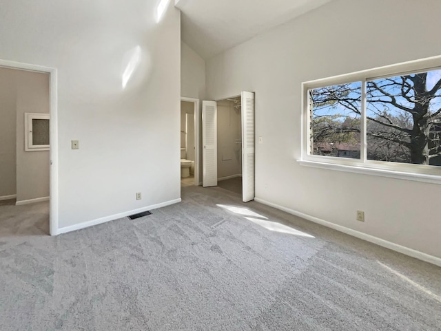 unfurnished bedroom with carpet, visible vents, ensuite bath, high vaulted ceiling, and baseboards