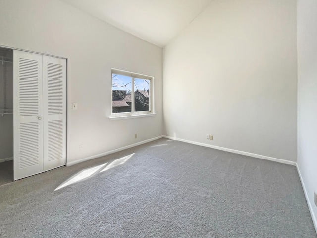 unfurnished bedroom featuring dark colored carpet, a closet, high vaulted ceiling, and baseboards