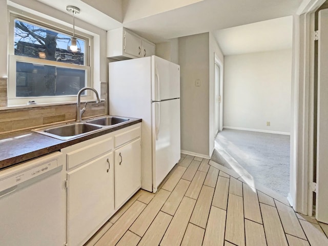 kitchen featuring white appliances, wood finish floors, a sink, dark countertops, and pendant lighting