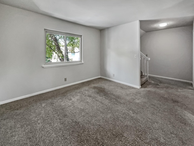 carpeted empty room featuring stairs and baseboards