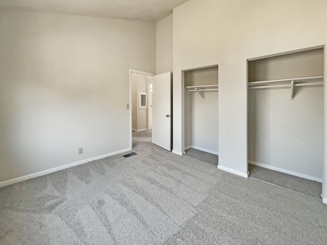 unfurnished bedroom with high vaulted ceiling, baseboards, two closets, and carpet flooring