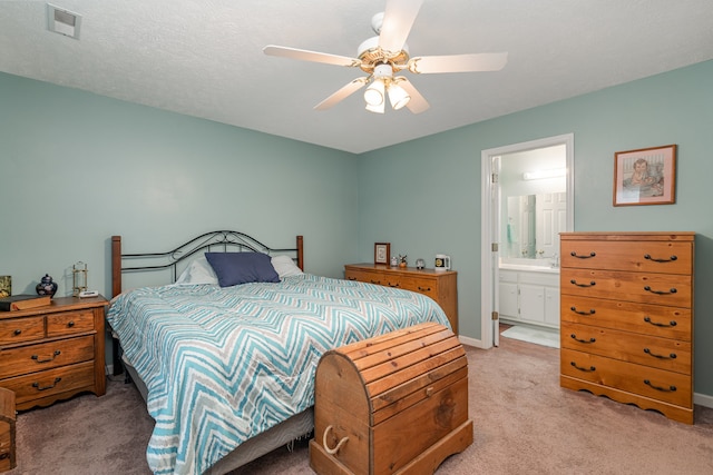 carpeted bedroom with a textured ceiling, ensuite bath, and ceiling fan