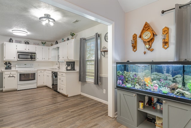 kitchen featuring black dishwasher, sink, electric stove, hardwood / wood-style floors, and white cabinetry