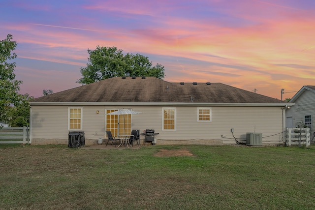 back house at dusk featuring a yard, a patio area, and central AC unit