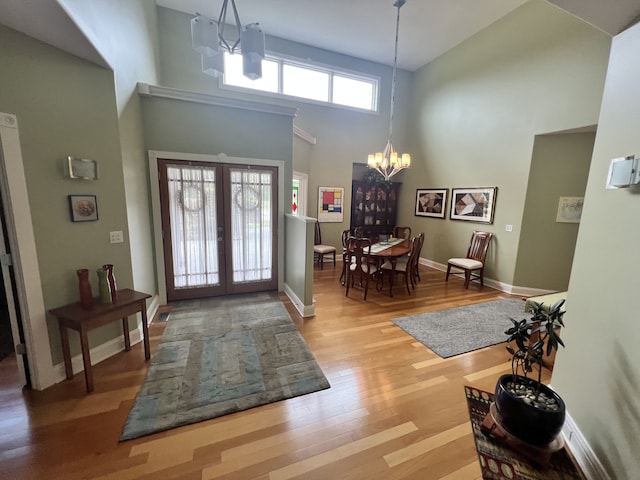 foyer with light wood-type flooring, french doors, a notable chandelier, and a towering ceiling