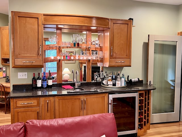 bar featuring dark stone counters, light hardwood / wood-style floors, wine cooler, and sink