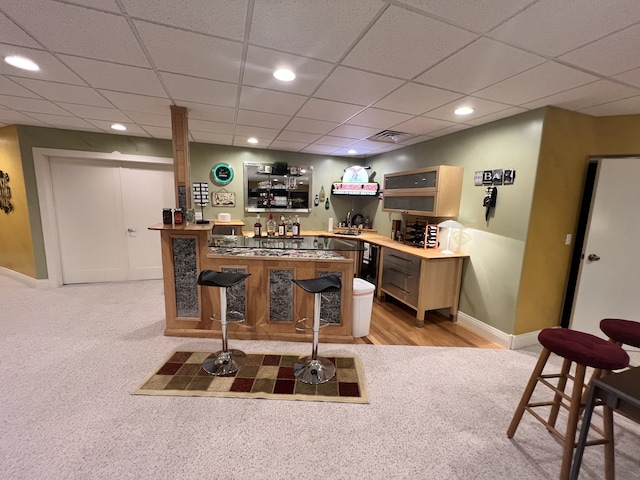 bar with light carpet, light brown cabinets, and a drop ceiling