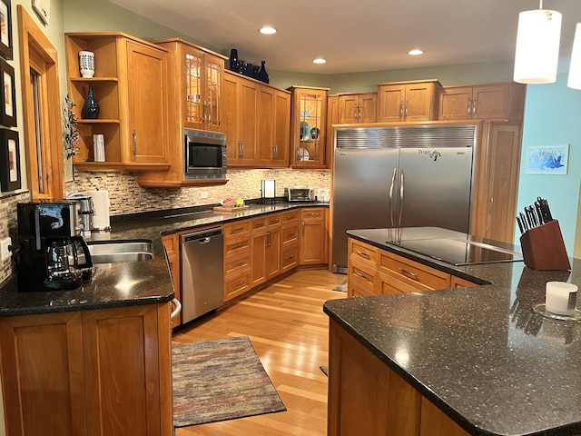 kitchen featuring built in appliances, decorative light fixtures, light hardwood / wood-style flooring, decorative backsplash, and dark stone countertops