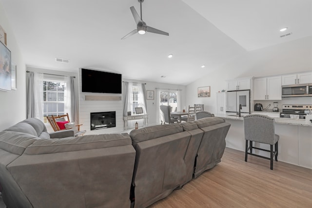 living room featuring vaulted ceiling, light hardwood / wood-style flooring, a large fireplace, sink, and ceiling fan