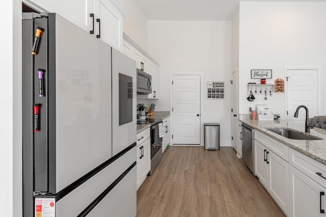 kitchen featuring light wood-type flooring, white cabinetry, sink, light stone countertops, and appliances with stainless steel finishes