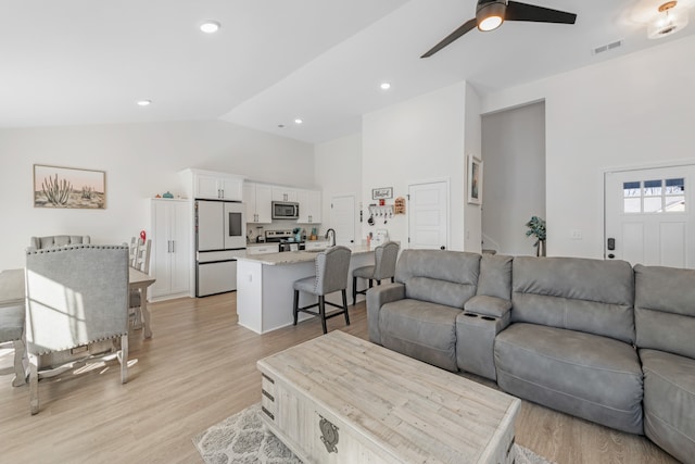 living room featuring light wood-type flooring, high vaulted ceiling, sink, and ceiling fan