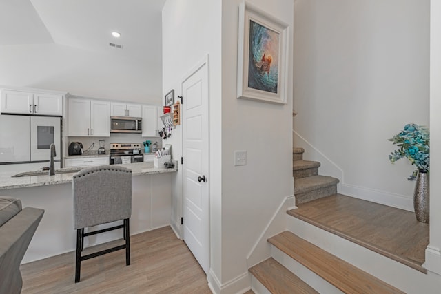 kitchen with a kitchen breakfast bar, appliances with stainless steel finishes, light hardwood / wood-style floors, white cabinetry, and light stone counters