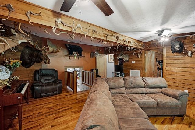 living room with ceiling fan, a textured ceiling, wooden walls, and wood-type flooring