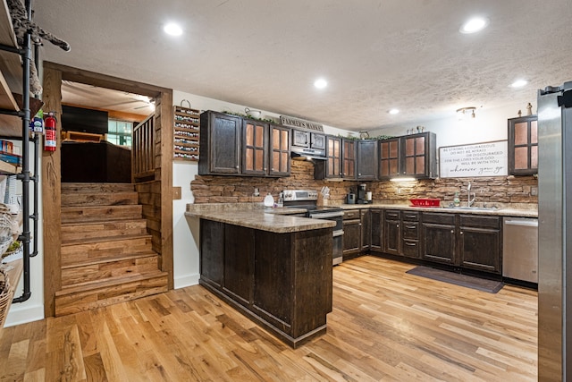 kitchen with kitchen peninsula, stainless steel appliances, a textured ceiling, dark brown cabinets, and light hardwood / wood-style flooring