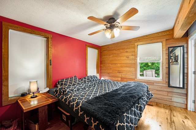 bedroom with ceiling fan, a textured ceiling, wood walls, and hardwood / wood-style floors