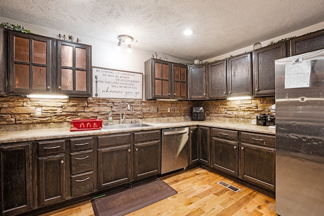 kitchen with appliances with stainless steel finishes, a textured ceiling, light hardwood / wood-style floors, and sink