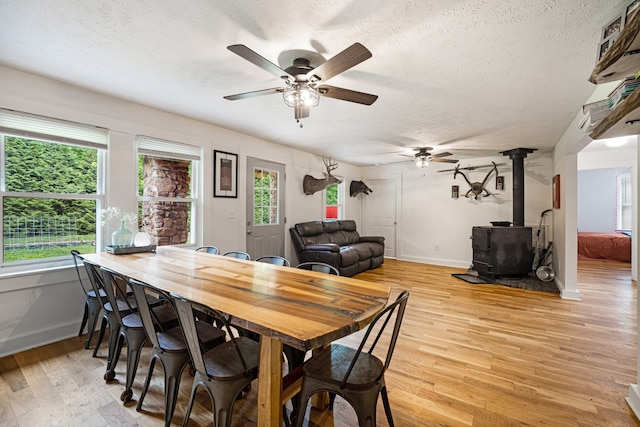 dining space with ceiling fan, plenty of natural light, light hardwood / wood-style floors, and a wood stove