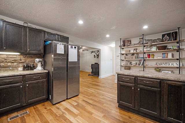 kitchen with dark brown cabinets, a textured ceiling, light wood-type flooring, and stainless steel fridge