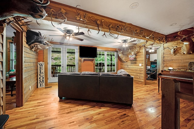 living room featuring light wood-type flooring, wood walls, ceiling fan, and french doors