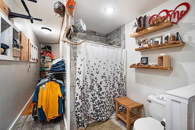 bathroom featuring a textured ceiling, wood-type flooring, toilet, and walk in shower