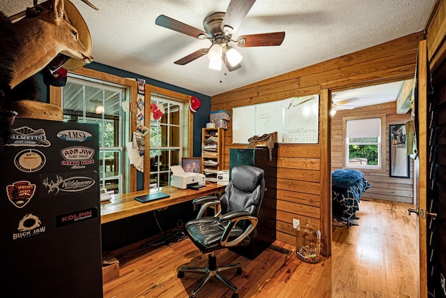 office space with ceiling fan, a textured ceiling, light hardwood / wood-style flooring, and wood walls