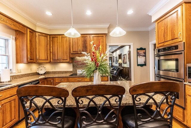 kitchen featuring a breakfast bar area, stone countertops, pendant lighting, ornamental molding, and double oven