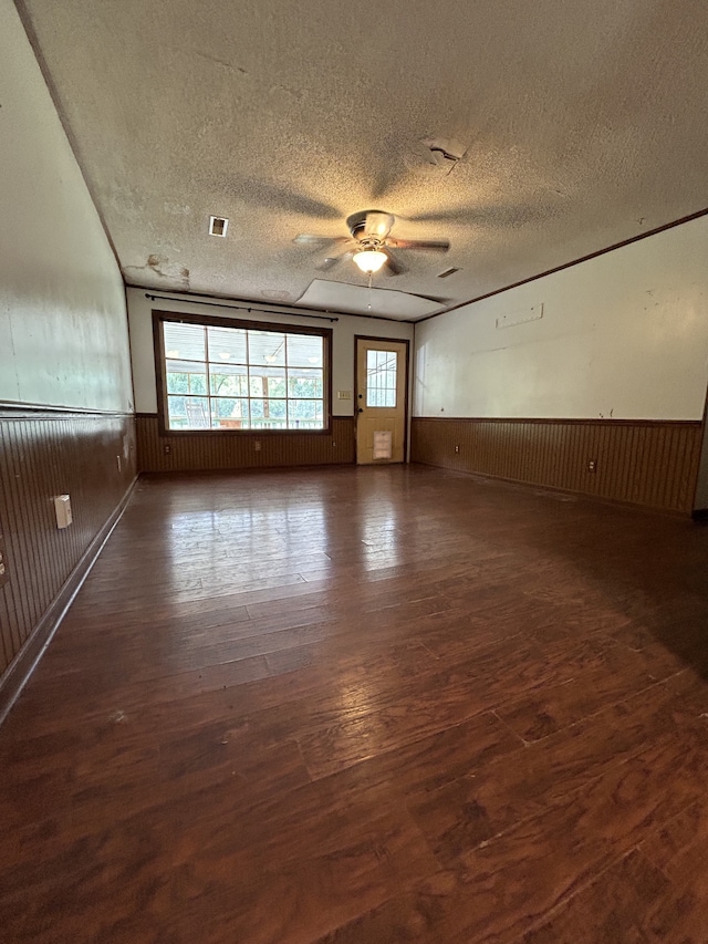 unfurnished room with dark hardwood / wood-style floors, wood walls, a textured ceiling, and ceiling fan