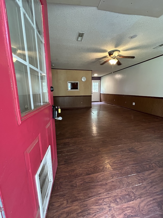 unfurnished room with a textured ceiling, ceiling fan, dark wood-type flooring, and wooden walls