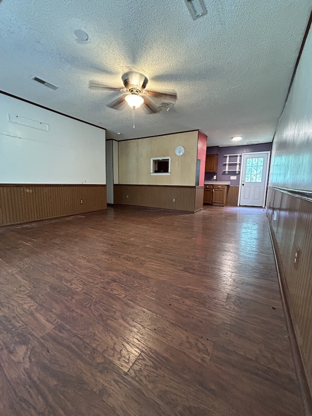 unfurnished living room featuring a textured ceiling, dark hardwood / wood-style flooring, ceiling fan, and wooden walls