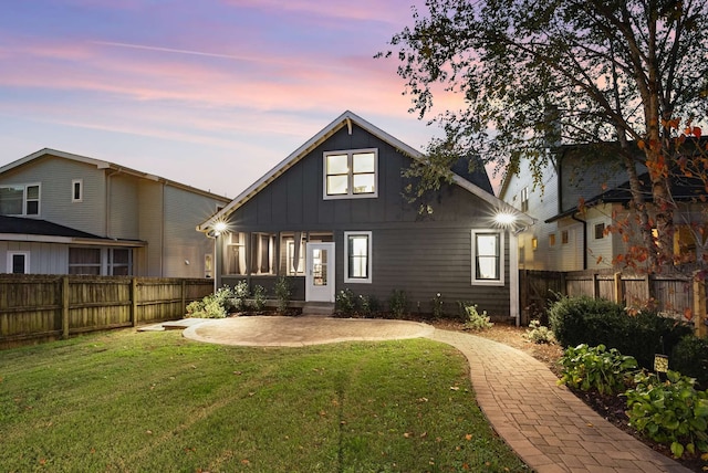 back house at dusk with a patio and a lawn