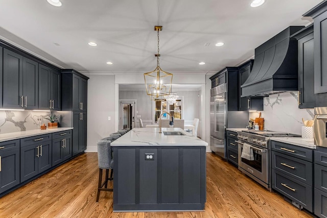 kitchen with premium range hood, sink, premium appliances, an island with sink, and pendant lighting