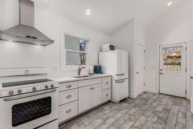 kitchen with ventilation hood, white cabinetry, sink, white appliances, and light hardwood / wood-style flooring