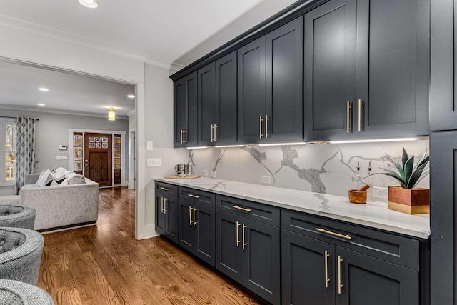 kitchen with ornamental molding, dark wood-type flooring, backsplash, and light stone counters