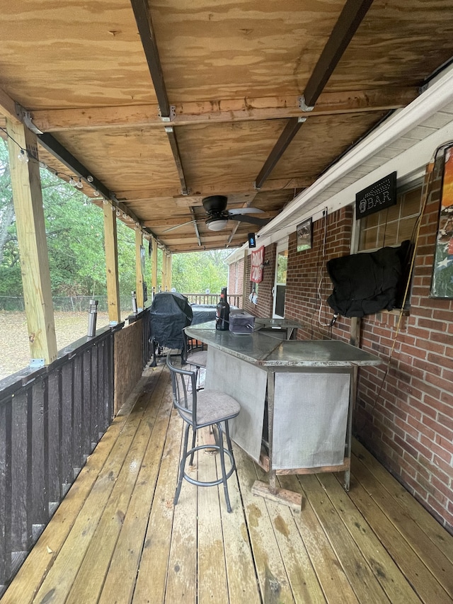 wooden terrace with area for grilling, ceiling fan, and exterior bar