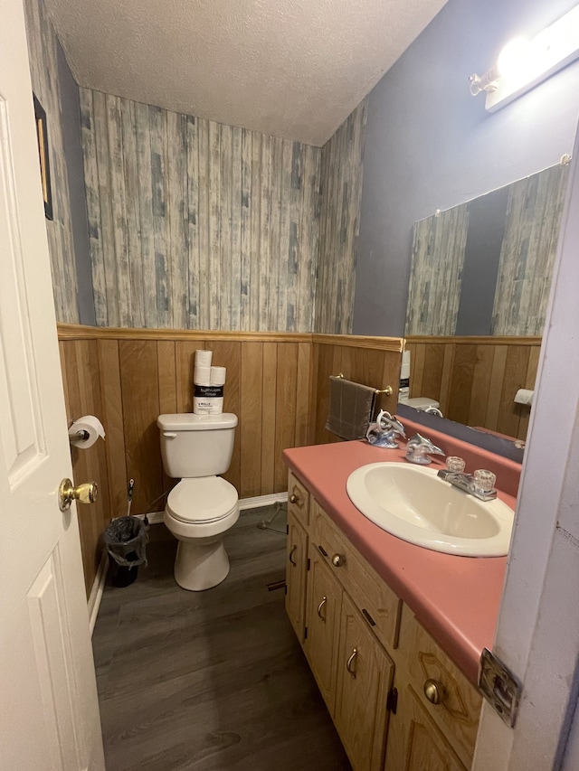 bathroom featuring toilet, wooden walls, vanity, a textured ceiling, and hardwood / wood-style flooring