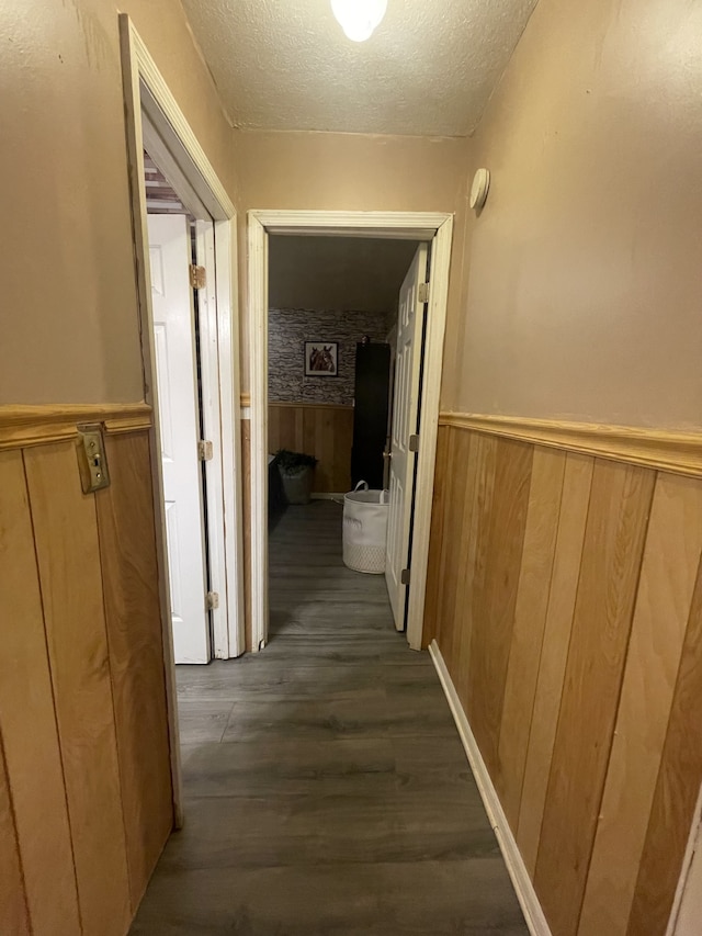 corridor featuring wooden walls, dark hardwood / wood-style floors, and a textured ceiling