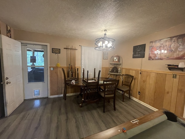 dining room with a textured ceiling, dark wood-type flooring, a notable chandelier, and wooden walls