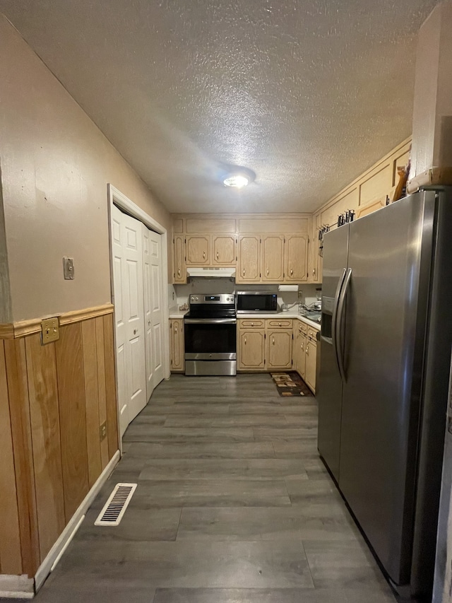 kitchen featuring wooden walls, a textured ceiling, dark hardwood / wood-style floors, appliances with stainless steel finishes, and light brown cabinets