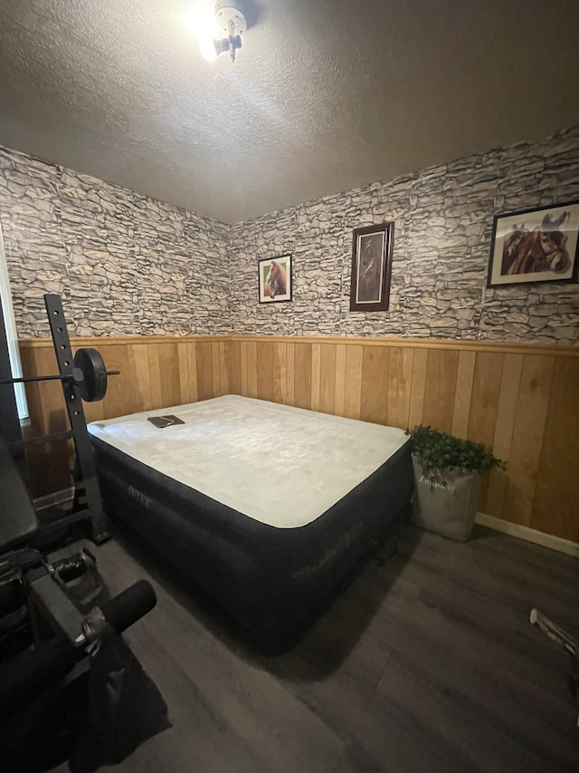 bedroom featuring a textured ceiling, wooden walls, and dark hardwood / wood-style floors