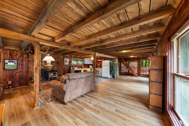 living room with beamed ceiling, wooden ceiling, a wood stove, light hardwood / wood-style flooring, and wooden walls