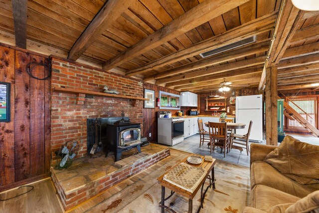 living room with wooden ceiling, light wood-type flooring, a wood stove, beamed ceiling, and ceiling fan