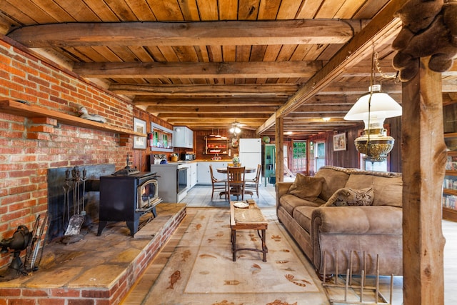 living room featuring wood ceiling, a wood stove, beam ceiling, and a brick fireplace