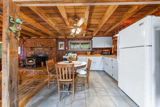 dining room featuring wooden ceiling, light tile patterned flooring, ceiling fan, and a wood stove