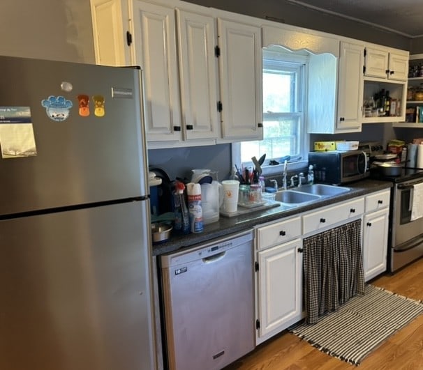 kitchen with appliances with stainless steel finishes, light hardwood / wood-style floors, white cabinetry, and sink