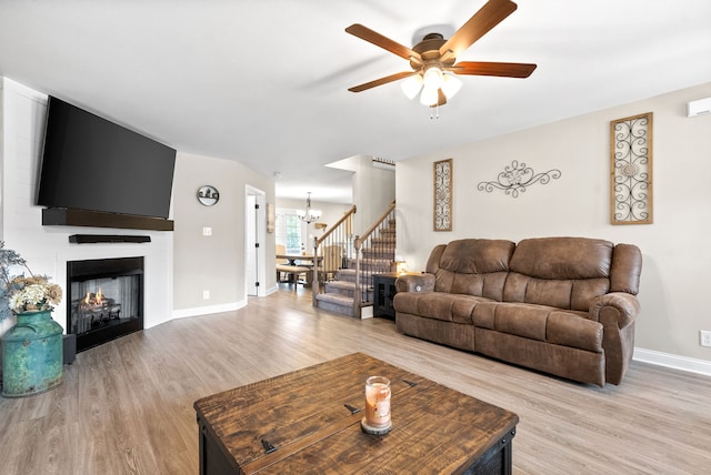 living room with a fireplace, ceiling fan with notable chandelier, and light hardwood / wood-style floors